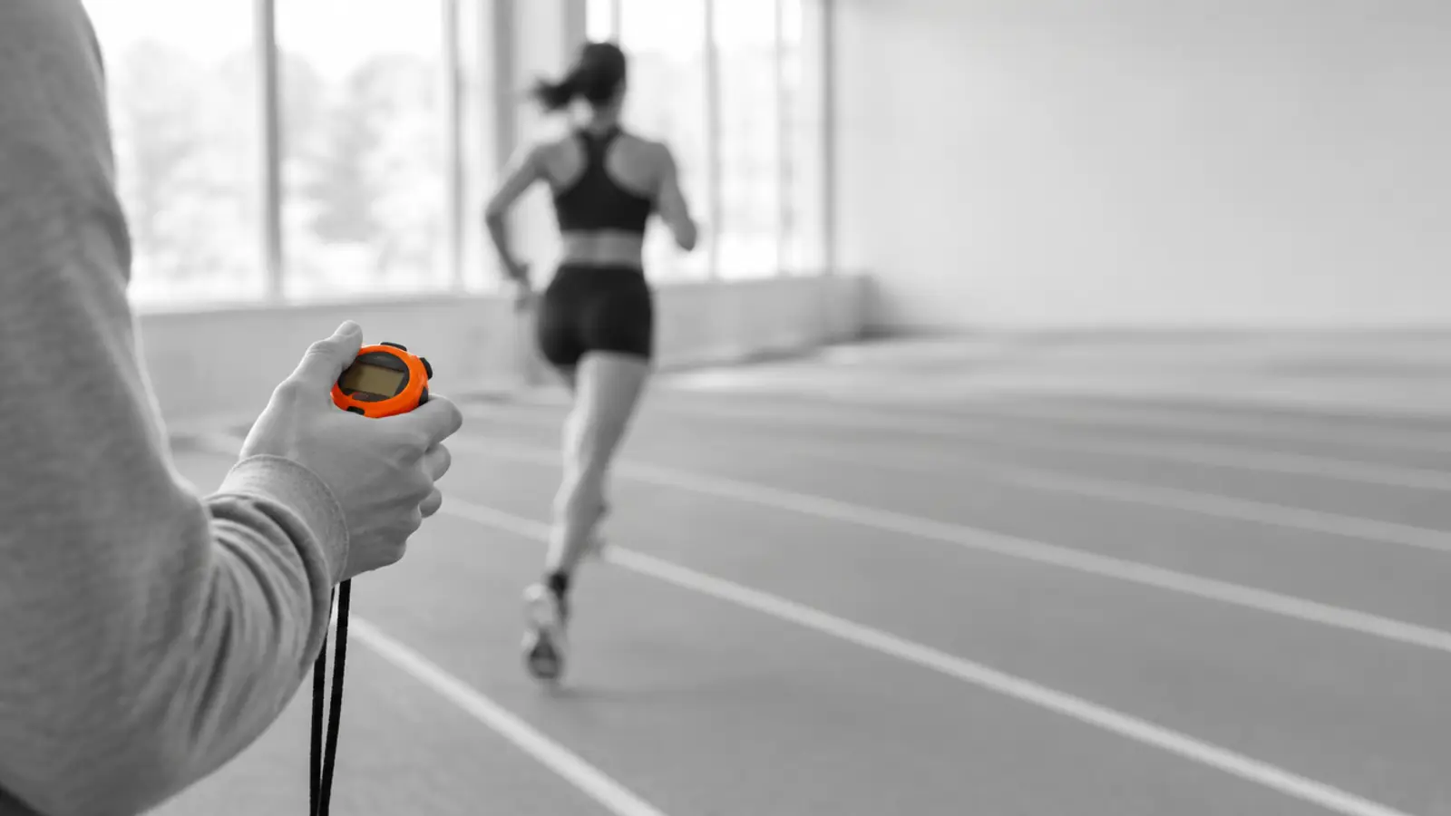 Coach holding a stopwatch while an athlete runs past
